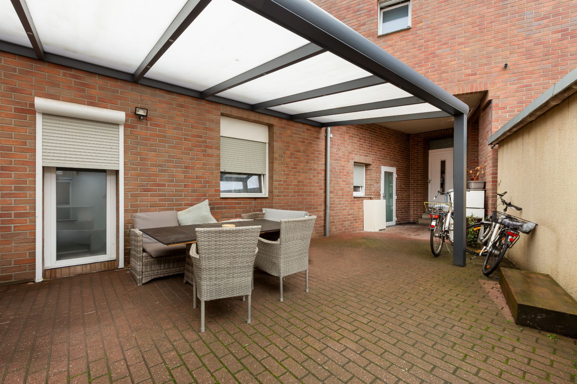 Überdachte Terrasse mit Sitzgruppe, Fahrrädern und Backsteinwänden.