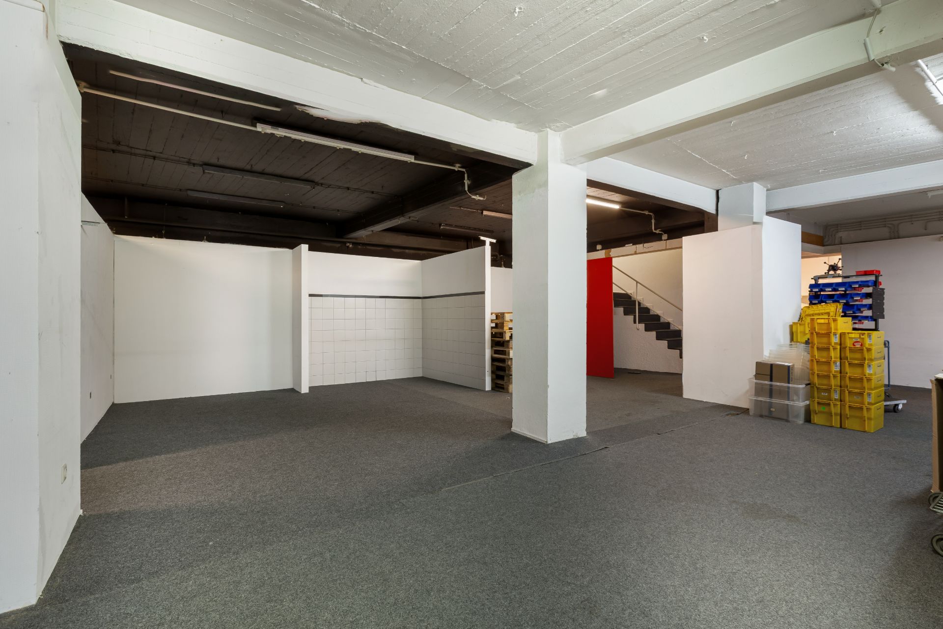 Großer Raum mit weißen Wänden, Teppichboden, Treppe und mehreren gestapelten gelben Kisten.