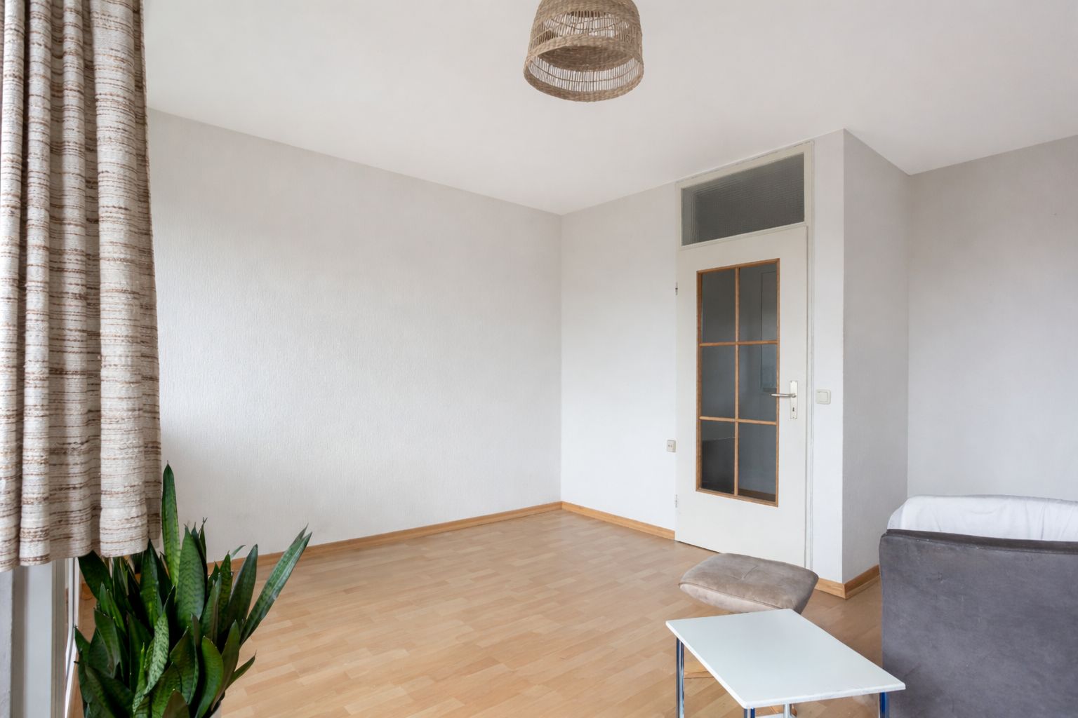 Helles Wohnzimmer mit Holzboden, Pflanze, Tisch, Sessel, Sofa und Tür.
