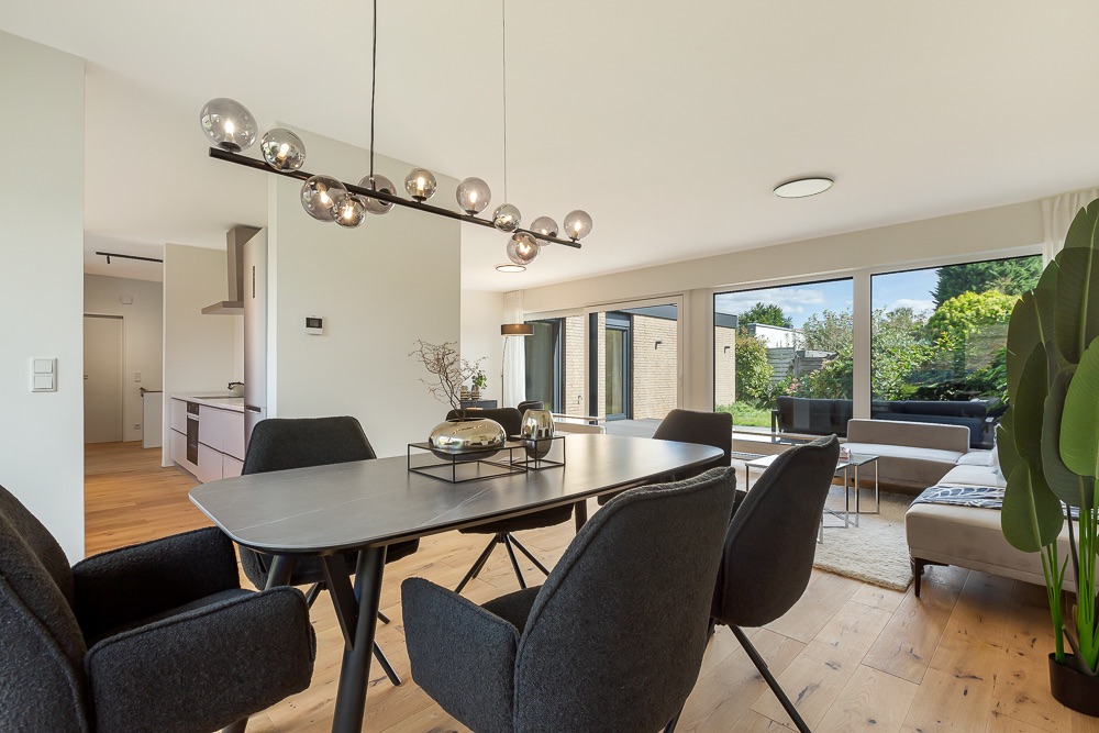 Modernes Esszimmer mit schwarzem Tisch, Stühlen und Blick ins helle Wohnzimmer mit großen Fenstern.