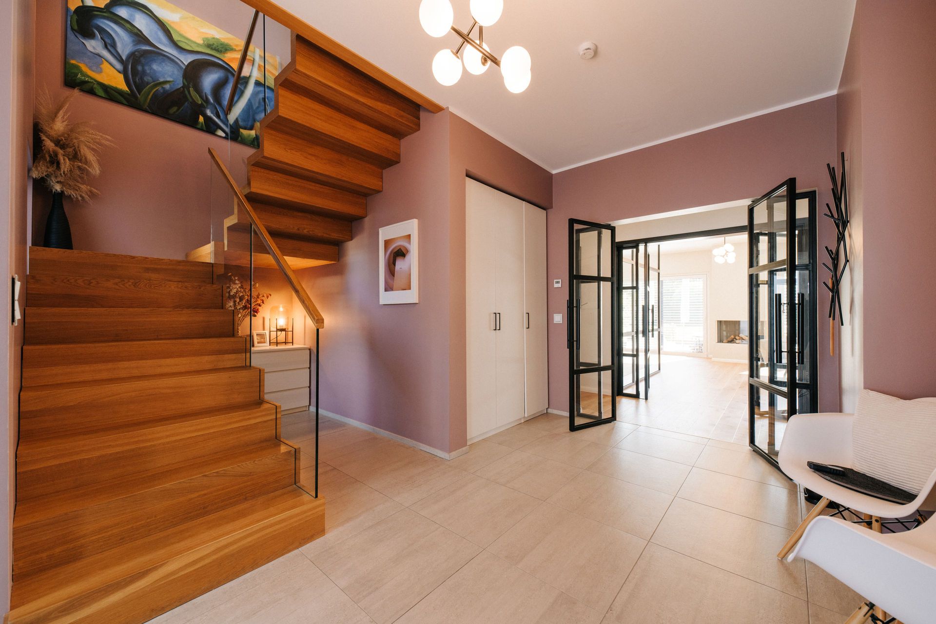 Moderner Eingangsbereich mit Holztreppe, Glastüren, Kunstwerken und beiger Bodenfliese.