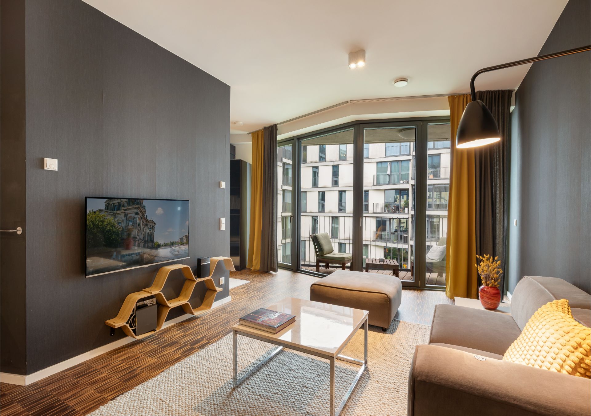 Modernes Wohnzimmer mit grauer Couch, großem Fenster und TV an der Wand.