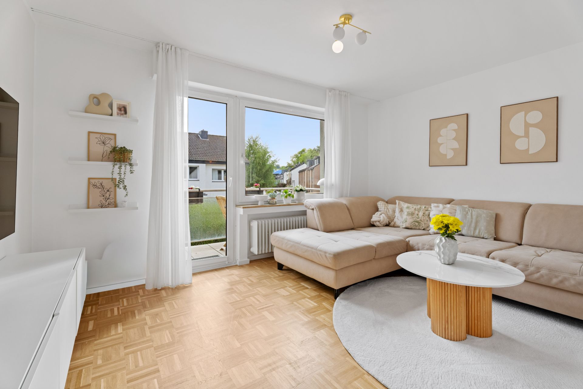 Helles Wohnzimmer mit beiger Eckcouch, Couchtisch, Parkettboden und großem Fenster mit Blick nach draußen.