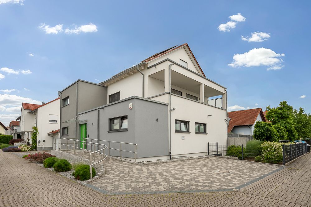 Modernes zweistöckiges Wohnhaus mit Balkon, Rampe und gepflasterter Einfahrt.