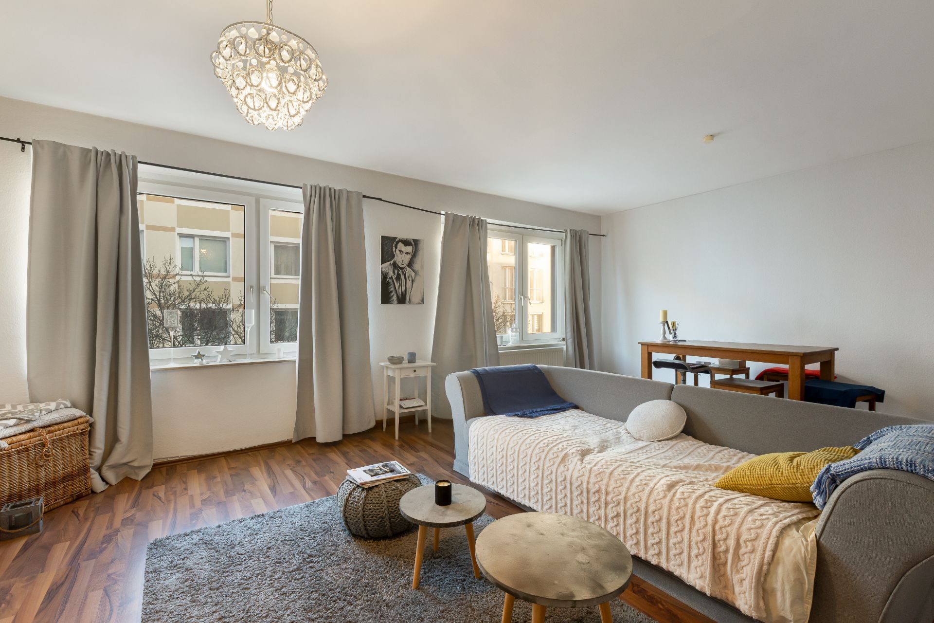 Helles Wohnzimmer mit grauem Sofa, Teppich, Couchtischen und großem Fenster.