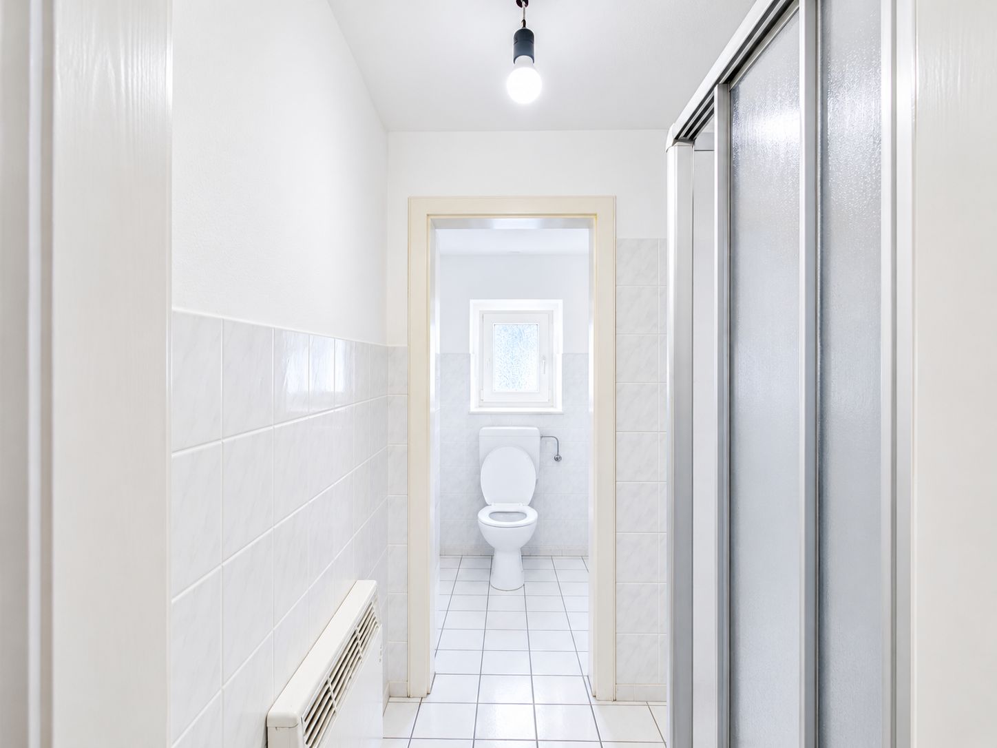 Helles Badezimmer mit Dusche rechts und Toilette am Fenster.