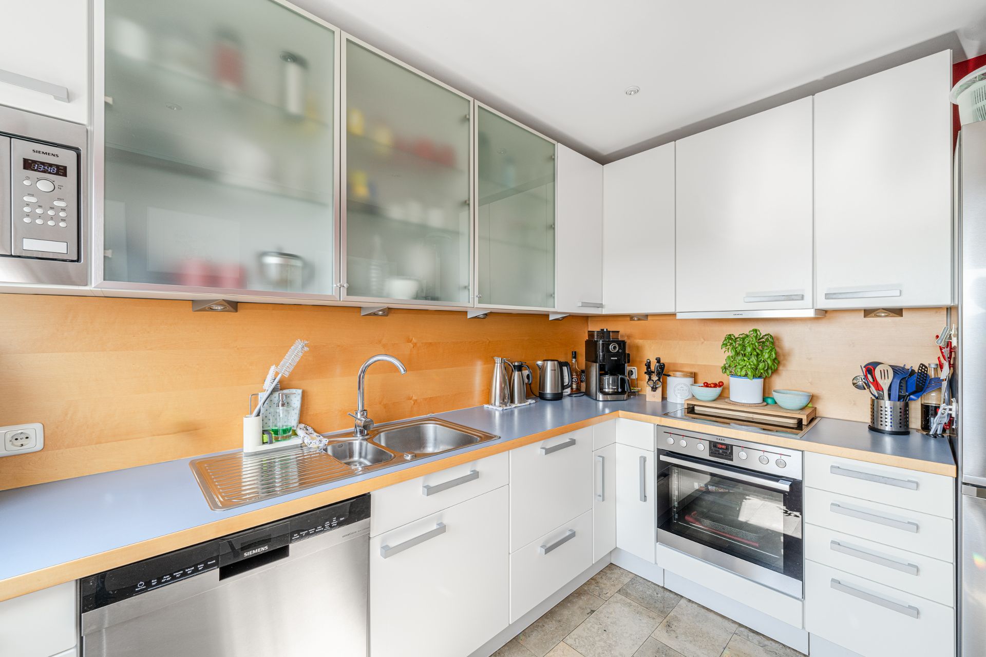 Moderne Einbauküche mit weißen Schränken, Herd, Spüle und Küchenutensilien.