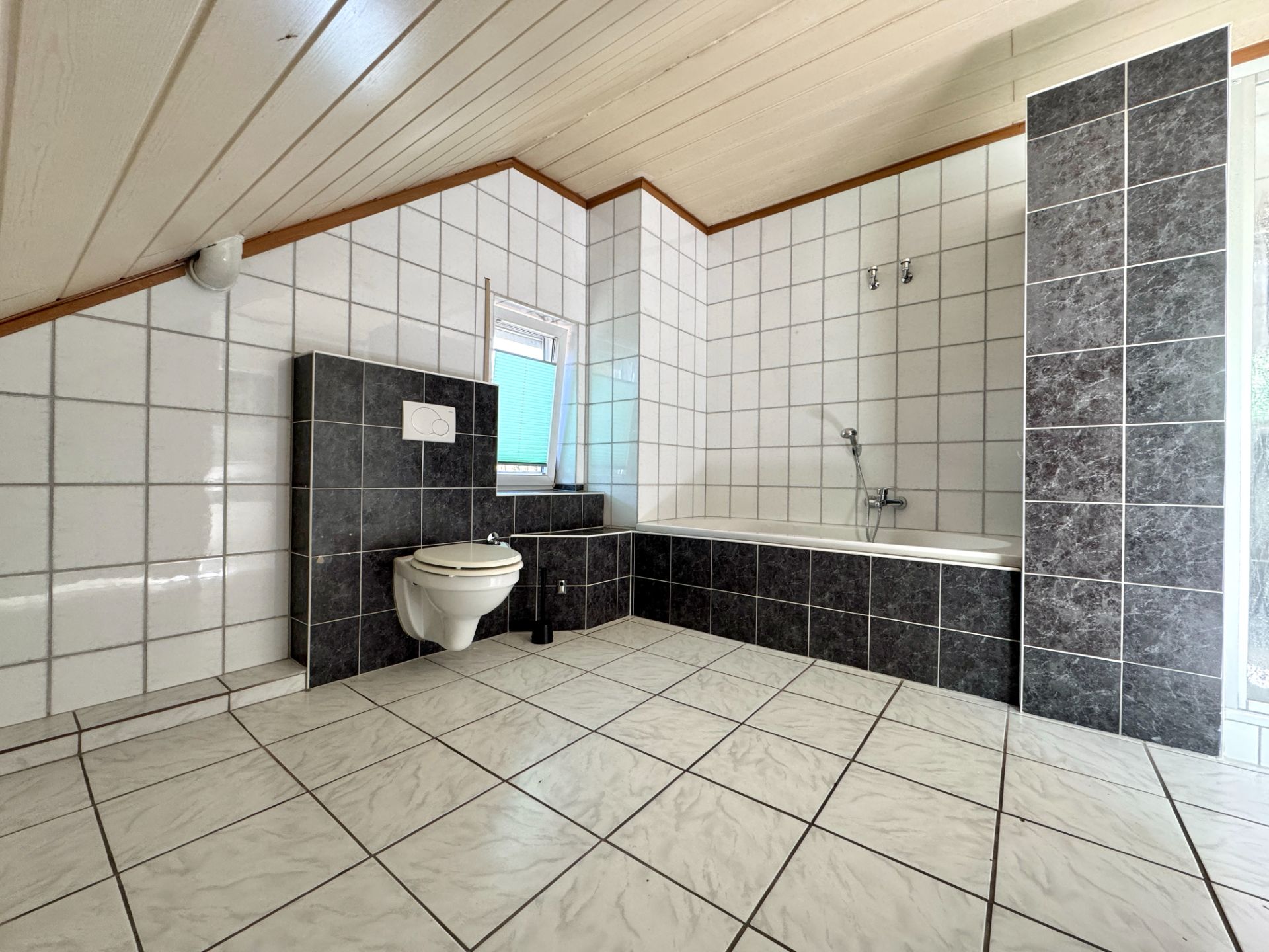 Modernes Badezimmer mit Badewanne, Toilette und weißen Fliesen an Wand und Boden.