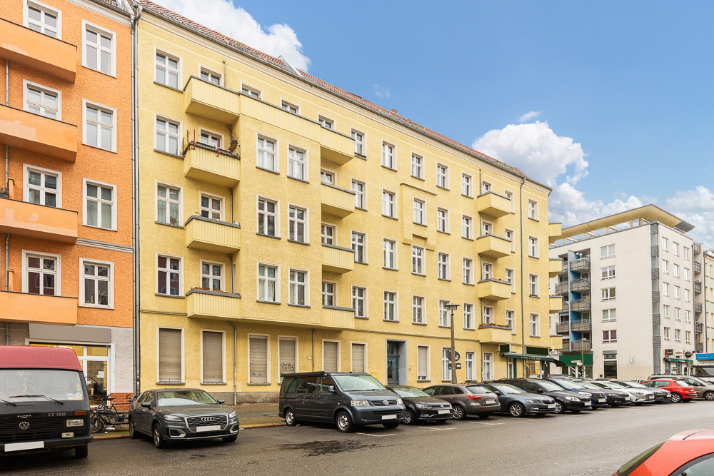 Mehrstöckiges Wohnhaus mit gelber Fassade, Balkonen und parkenden Autos davor.
