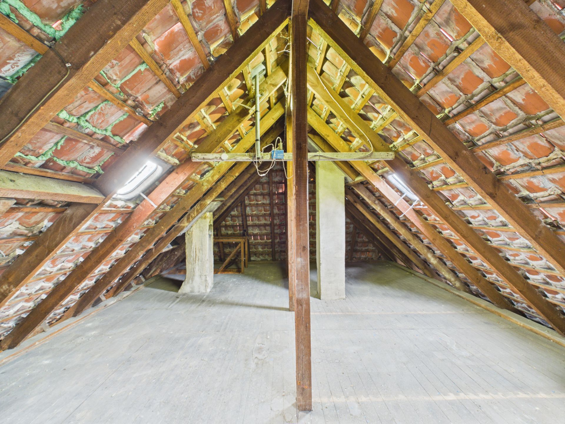 Dachboden mit sichtbarem Holzbalken, Ziegeln und Holzboden, Tageslicht fällt von beiden Seiten ein.