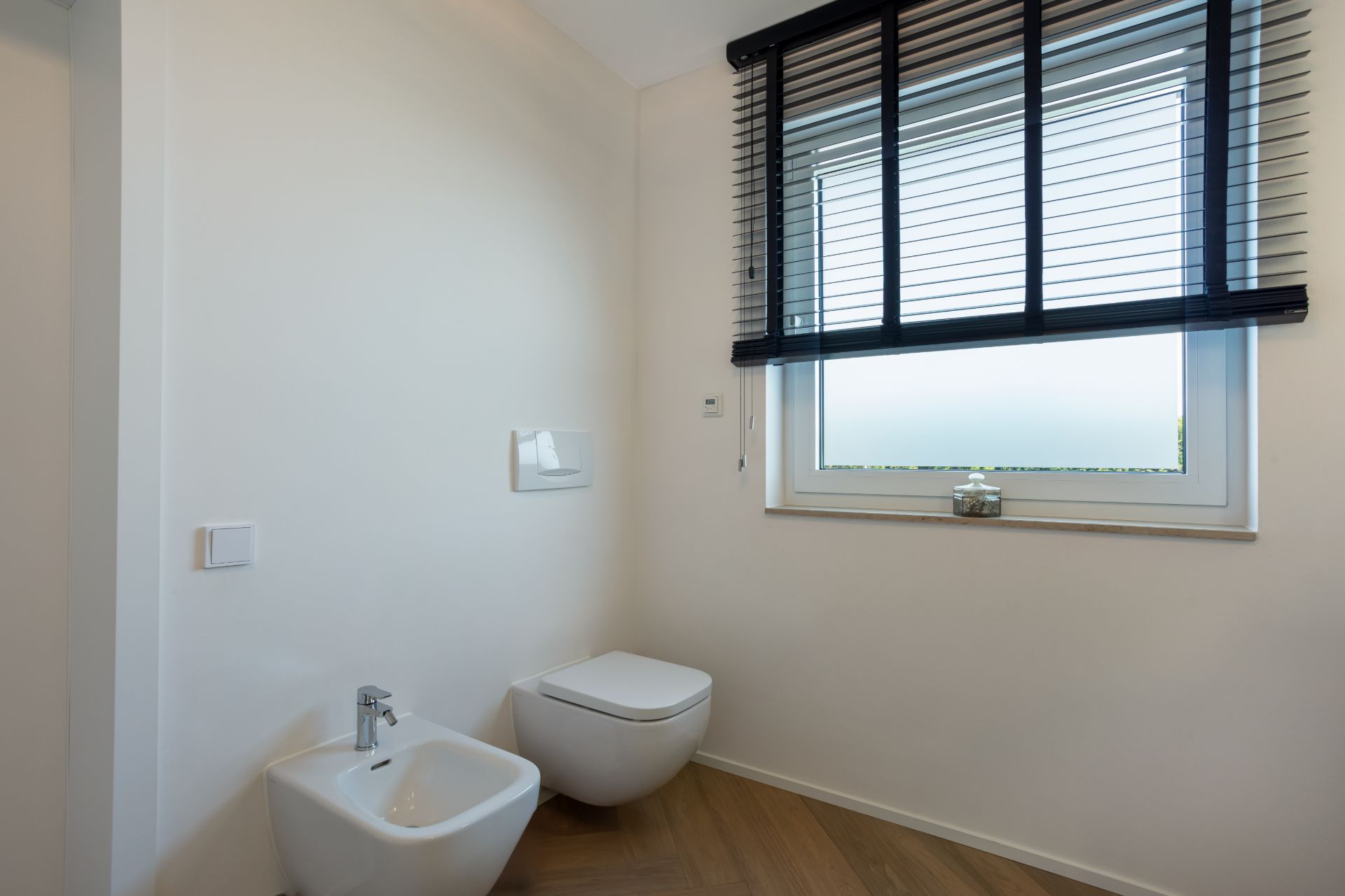 Modernes Badezimmer mit Wandtoilette, Bidet und Fenster mit Jalousien.