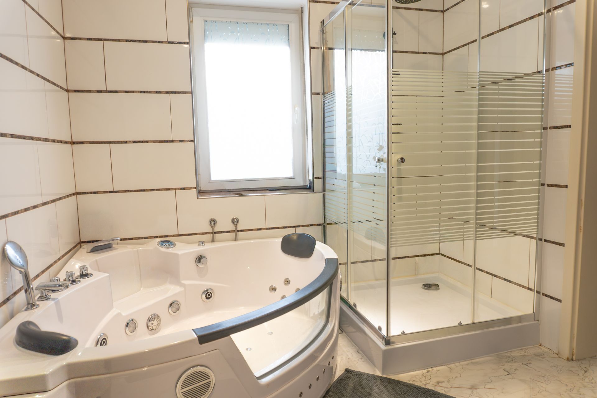 Badezimmer mit großer Eckbadewanne, Dusche und Fenster, alles gefliest.