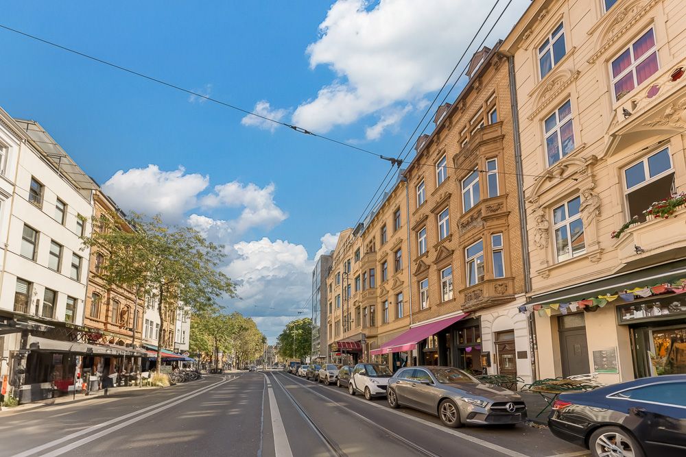 Straße mit parkenden Autos und mehreren Wohnhäusern bei blauem Himmel.