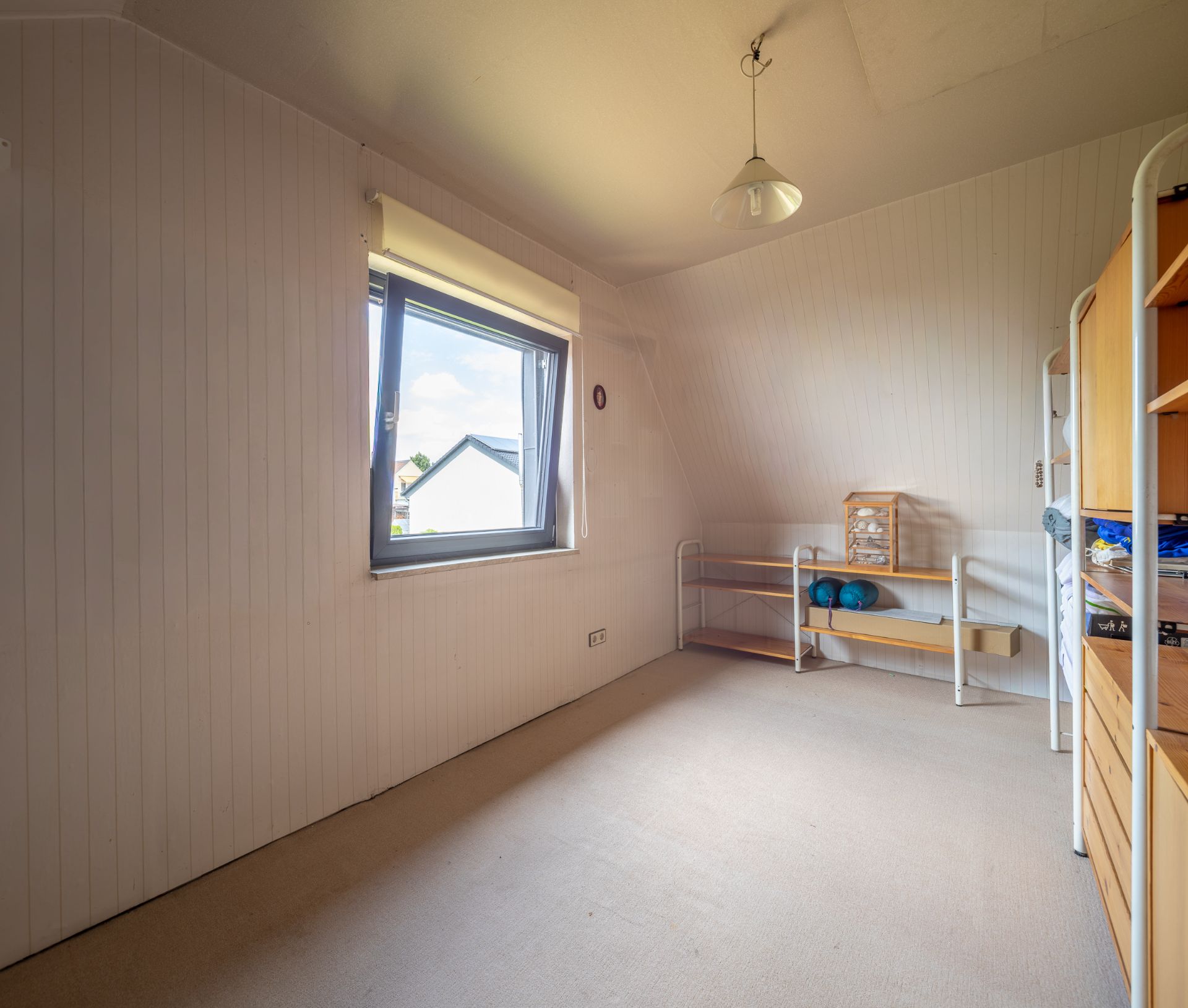 Helles Zimmer mit Fenster, Regal und kleinem Sideboard an der Wand.