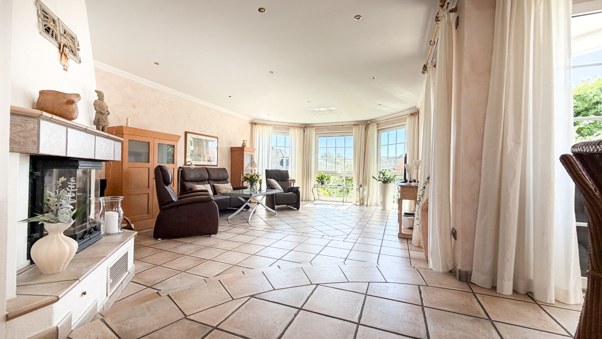 Helles Wohnzimmer mit großen Fenstern, zwei Sofas, Kamin und Fliesenboden.