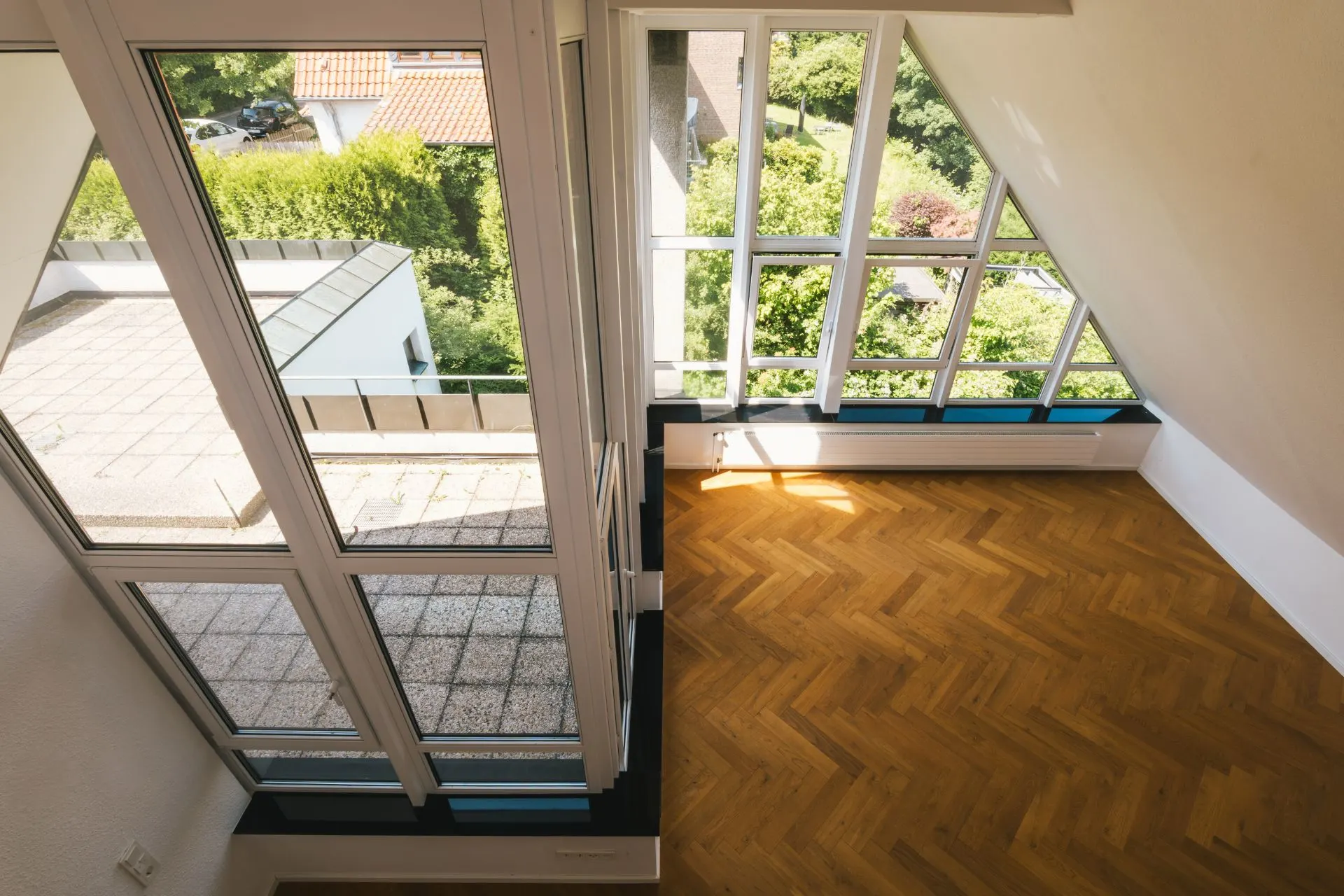 Heller Raum mit großen Fenstern, Parkettboden und Zugang zu einer Terrasse, Blick ins Grüne.