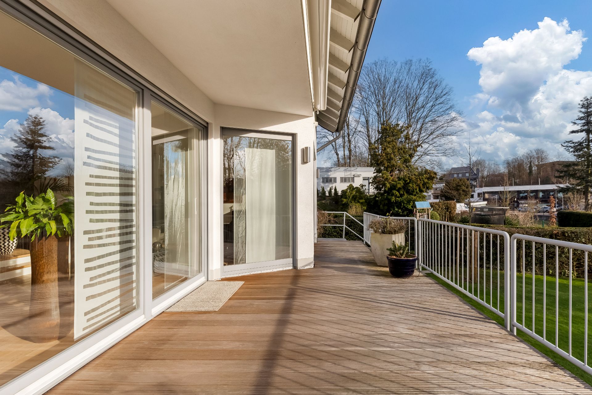 Große Terrasse mit Holzboden, Glasgeländer und Blick auf Garten und Bäume.