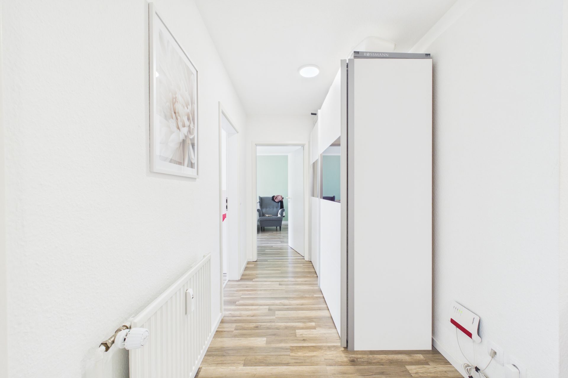 Heller Flur mit Holzfußboden, weißen Wänden und einem großen Schrank.