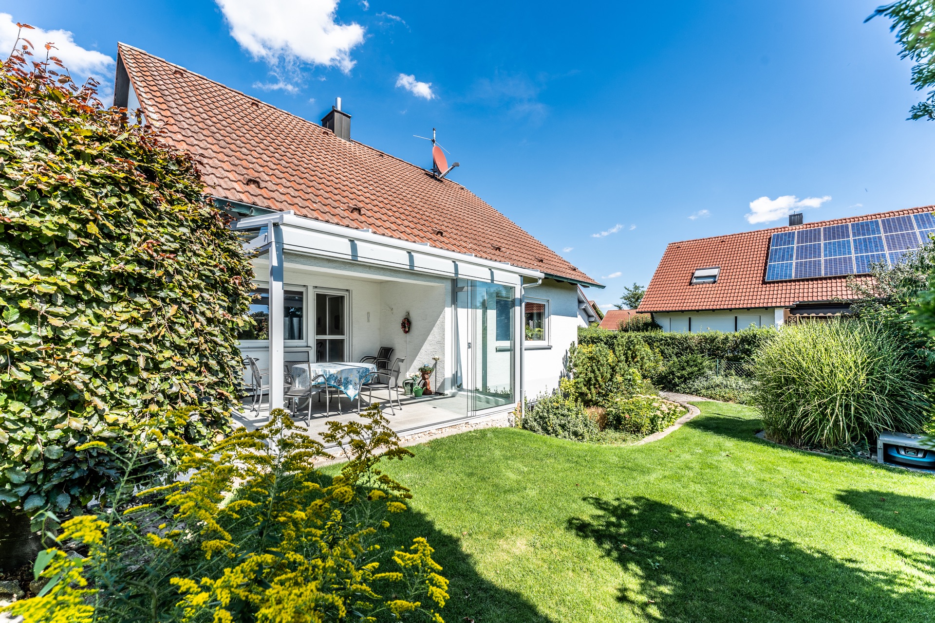 Einfamilienhaus mit Wintergarten, Terrasse und gepflegtem Garten bei sonnigem Wetter.