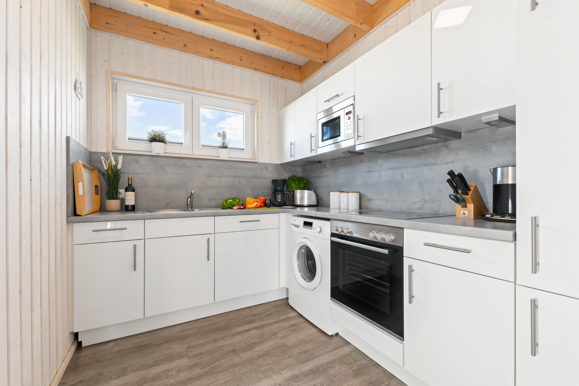 Moderne Küche mit weißen Schränken, Elektrogeräten und Holzdecke.