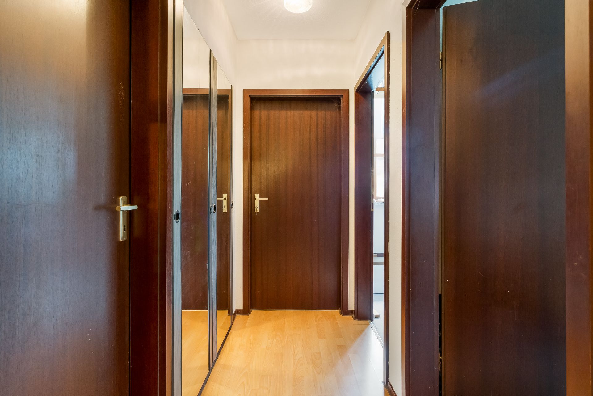 Flur mit Holztüren, Spiegel an der linken Wand und hellem Laminatboden.