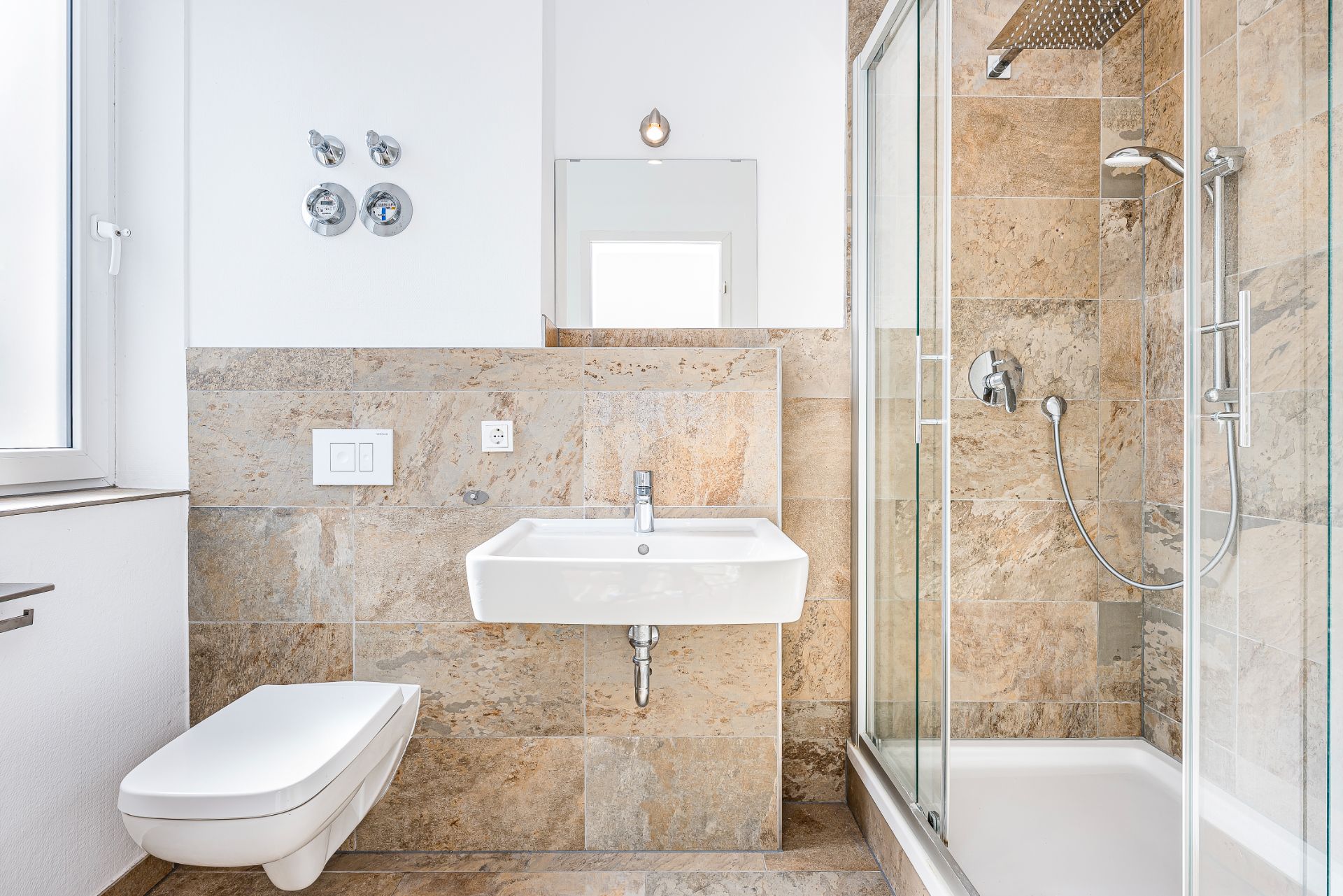 Modernes Bad mit Wandtoilette, Waschbecken und Glasdusche mit Regenduschkopf.