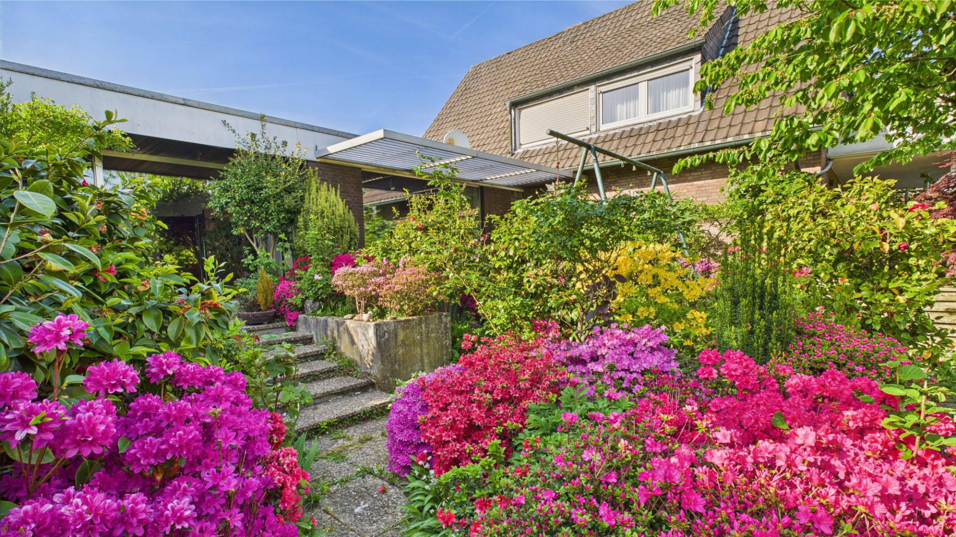Haus mit Garten, Treppe und vielen bunten Blumen und Sträuchern im Vordergrund.