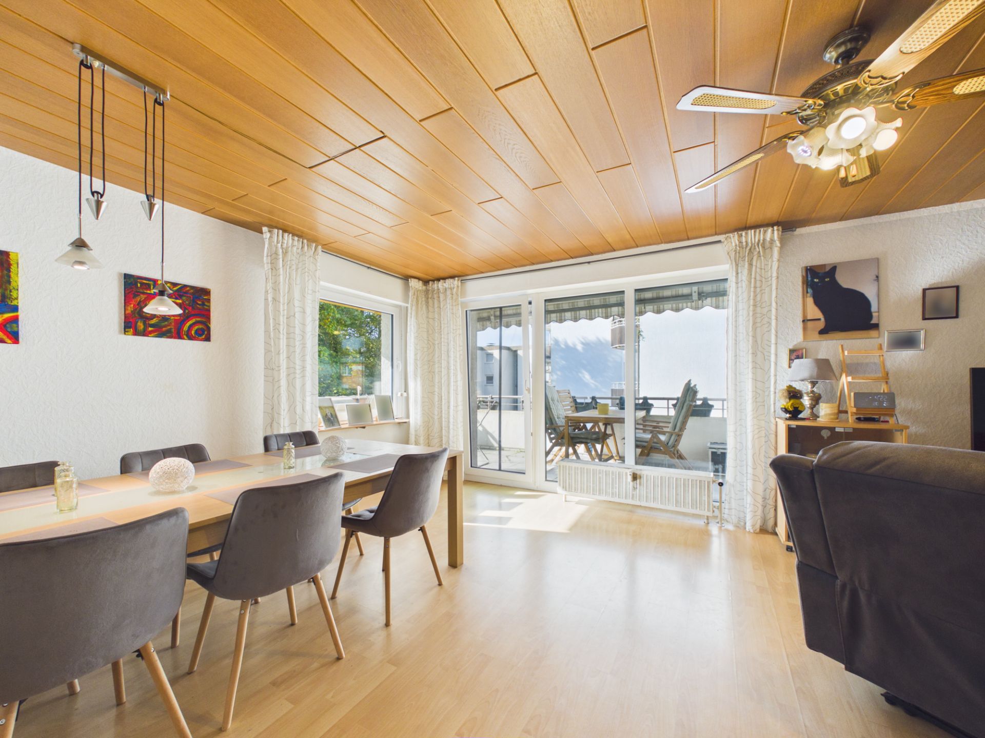 Helles Wohnzimmer mit Holzboden, großem Esstisch, Stühlen und Zugang zu einem Balkon mit Aussicht.