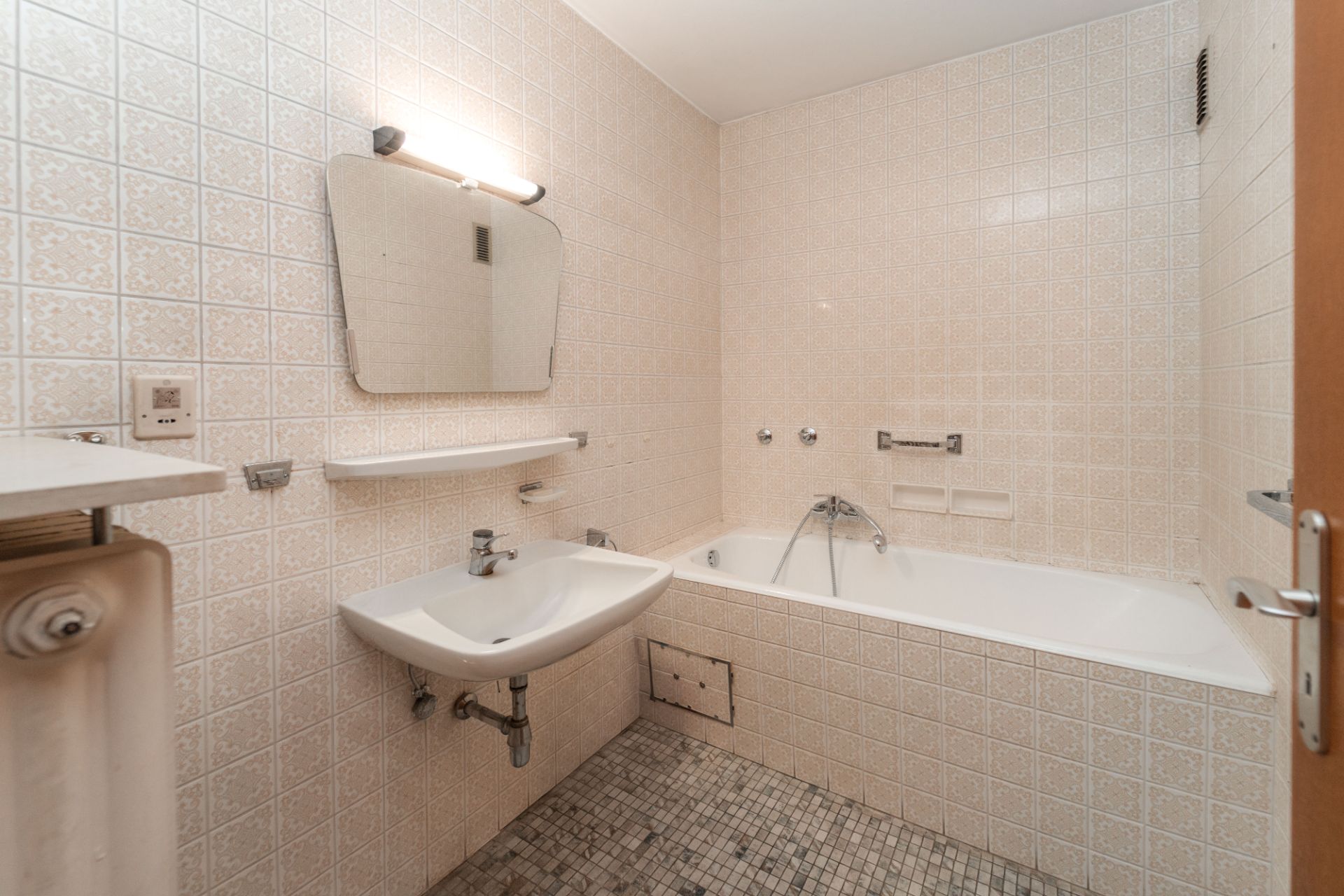 Kleines Badezimmer mit Badewanne, Waschbecken, Spiegel und hellen Fliesen.