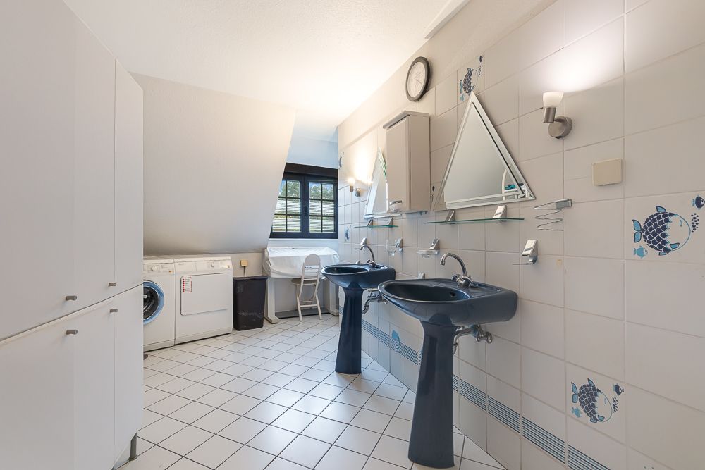 Helles Badezimmer mit zwei Waschbecken, Waschmaschine, Trockner und weißen Schränken.