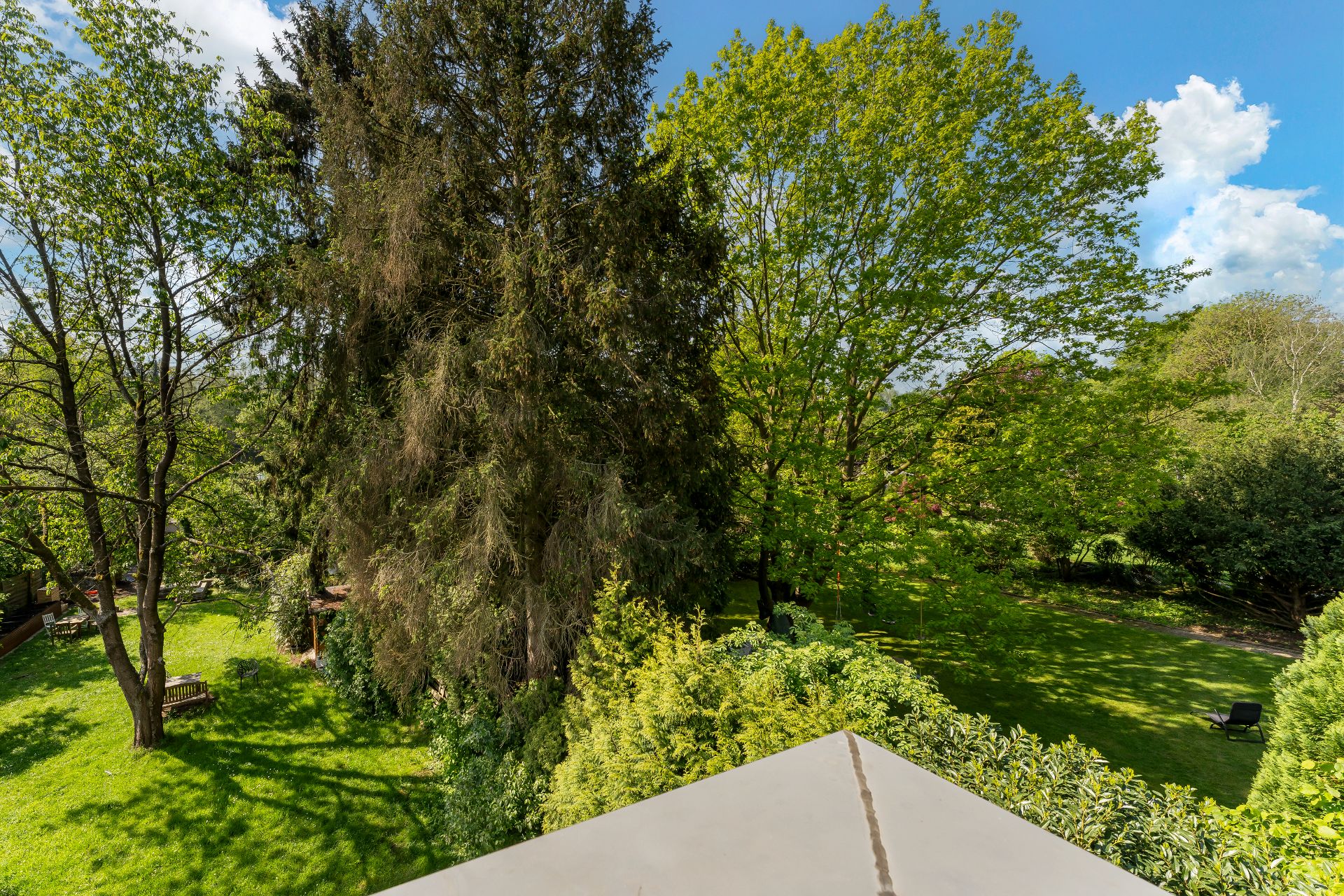 Blick auf einen großen, grünen Garten mit Rasen, Bäumen und einzelnen Sitzbänken.