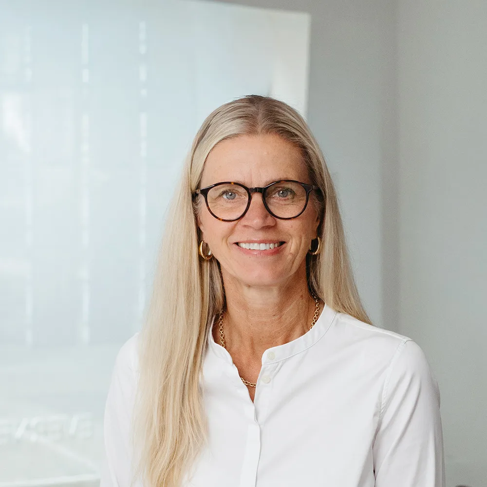 Frau mit langen blonden Haaren und Brille steht in einem modernen Raum.