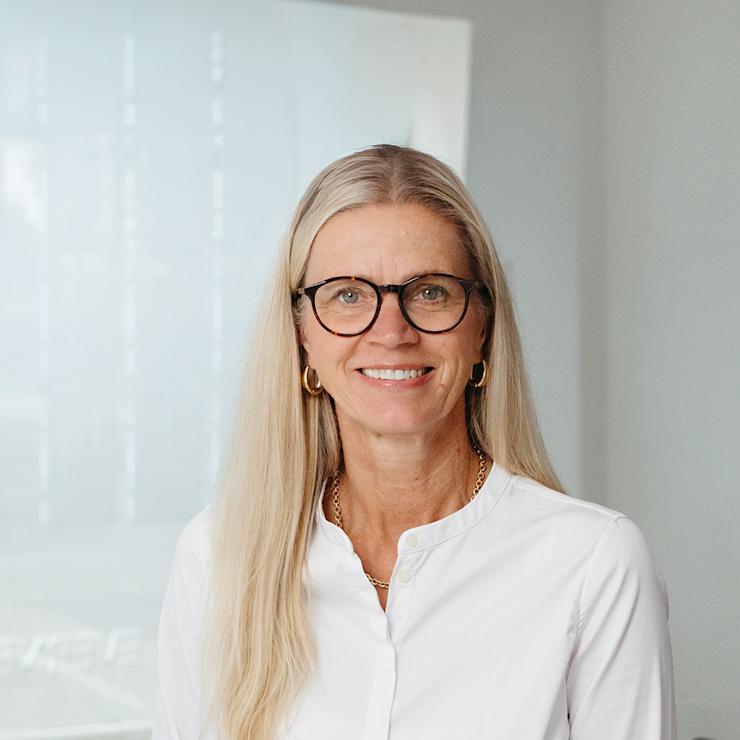 Frau mit langen blonden Haaren und Brille steht in einem modernen Raum.