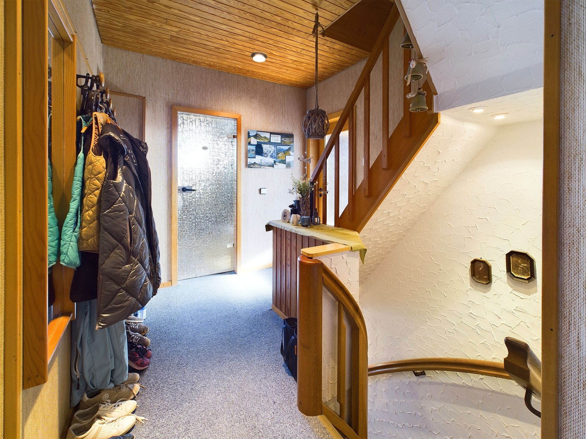 Flur mit Holztreppe, Garderobe mit Jacken und Schuhen, Holztäfelung an der Decke.