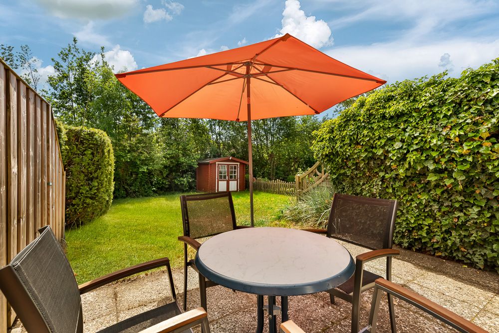 Runder Tisch mit vier Stühlen und orangefarbenem Sonnenschirm auf Terrasse im Garten.