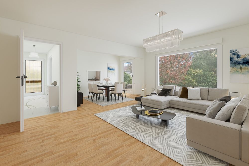 Helles Wohnzimmer mit Sofa, Teppich, Couchtisch und großem Fenster, Essbereich im Hintergrund.