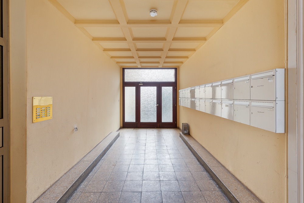 Heller Hausflur mit Briefkästen an der rechten Wand und Glastür am Ende.