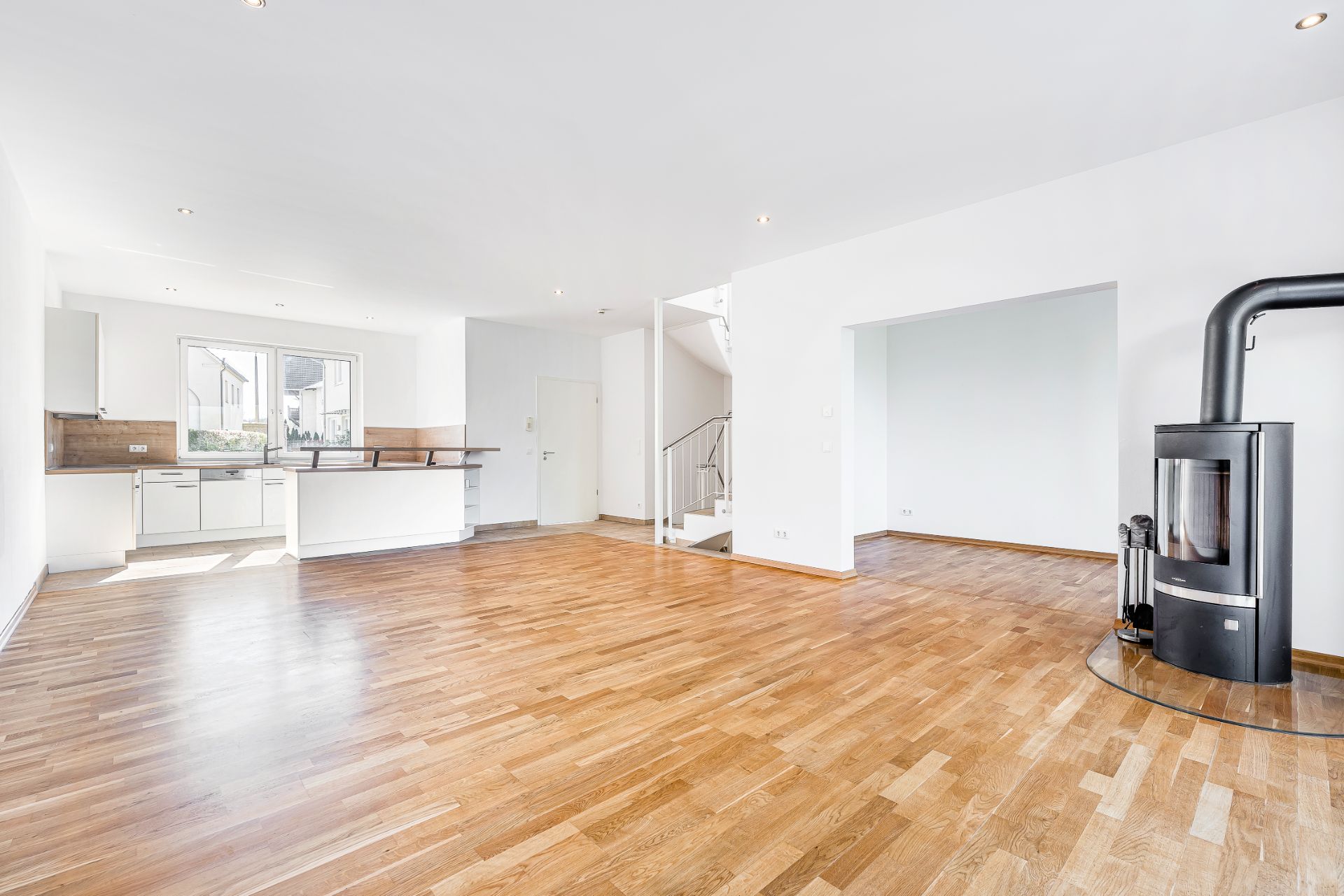 Heller Wohnraum mit Holzboden, offener Küche, Kaminofen und Treppe.