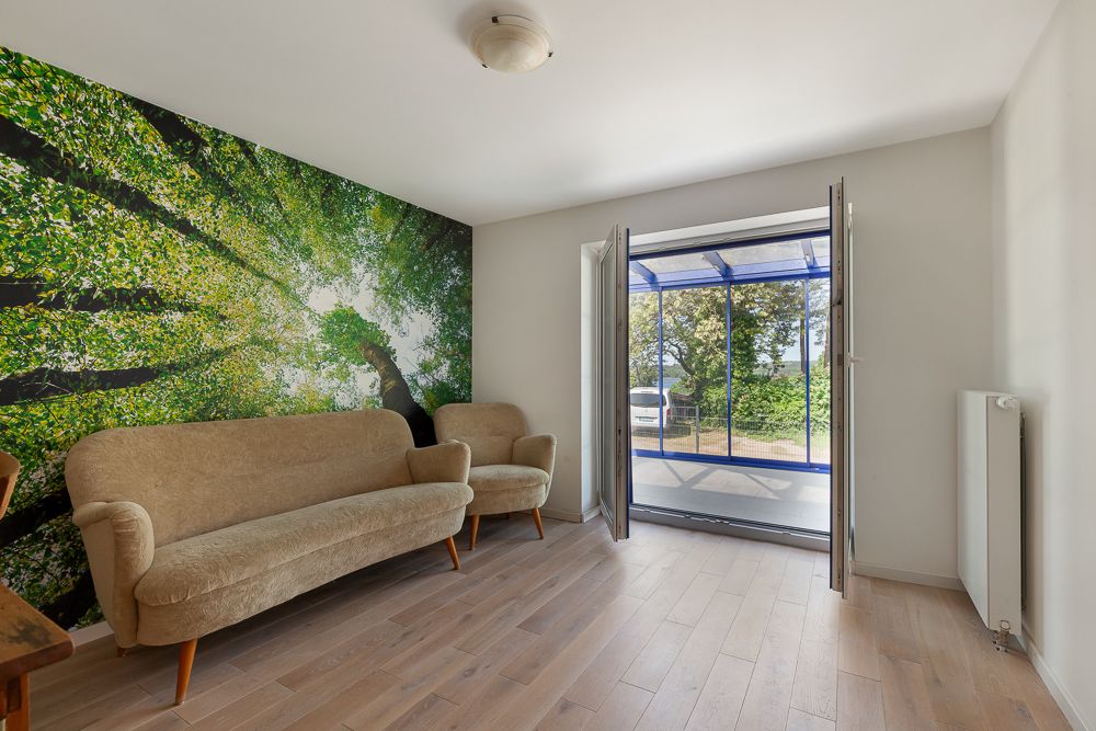 Wohnzimmer mit beigen Sofas, großem Baum-Wandbild und Zugang zu verglastem Balkon.