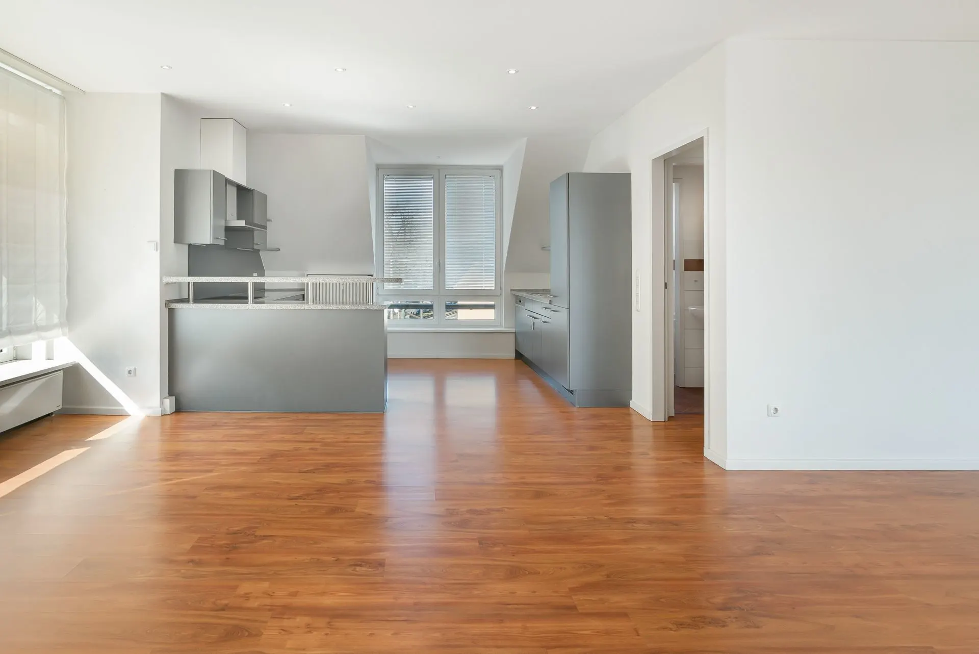 Helles Wohnzimmer mit Parkettboden, offener Küche und großen Fenstern.