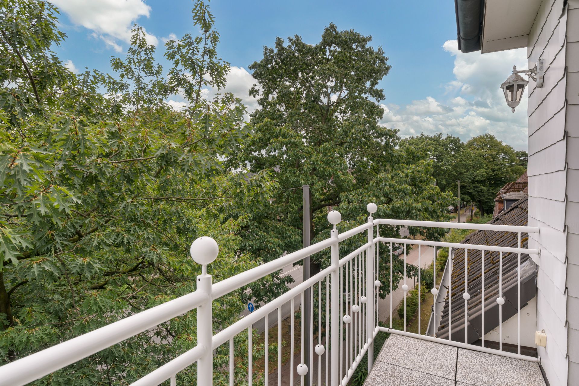 Ein Balkon mit weißem Geländer und Blick auf grüne Bäume und Straße.