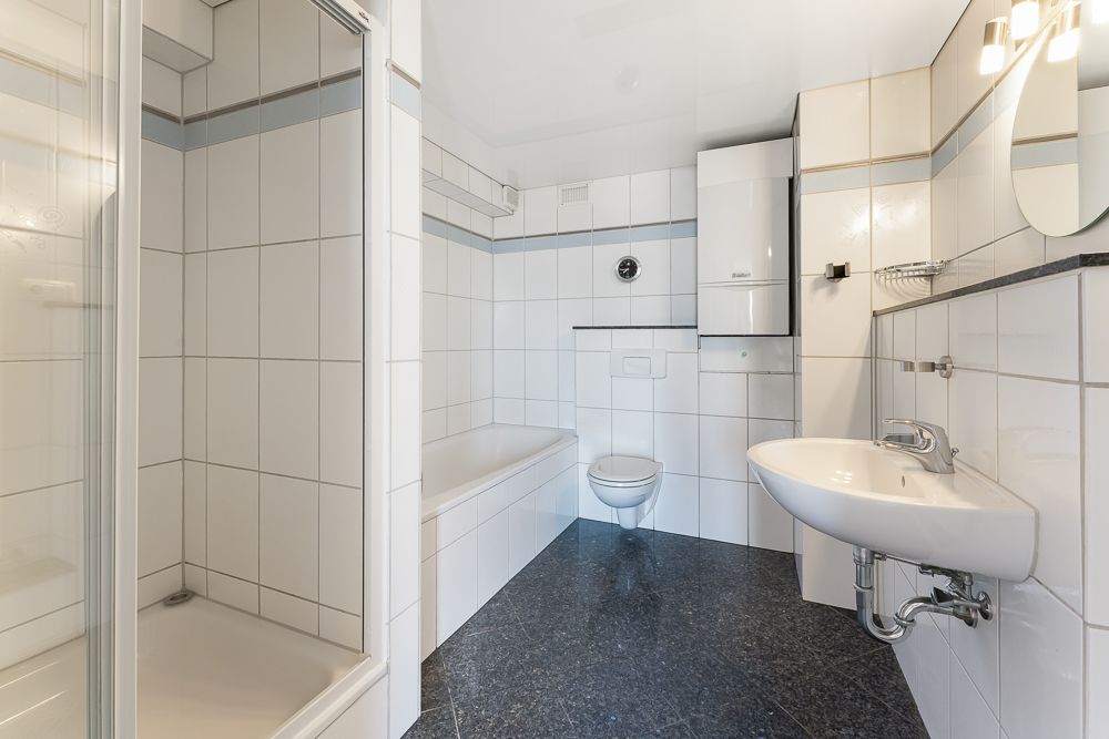 Helles Badezimmer mit Dusche, Badewanne, WC und Waschbecken, alles weiß gefliest.