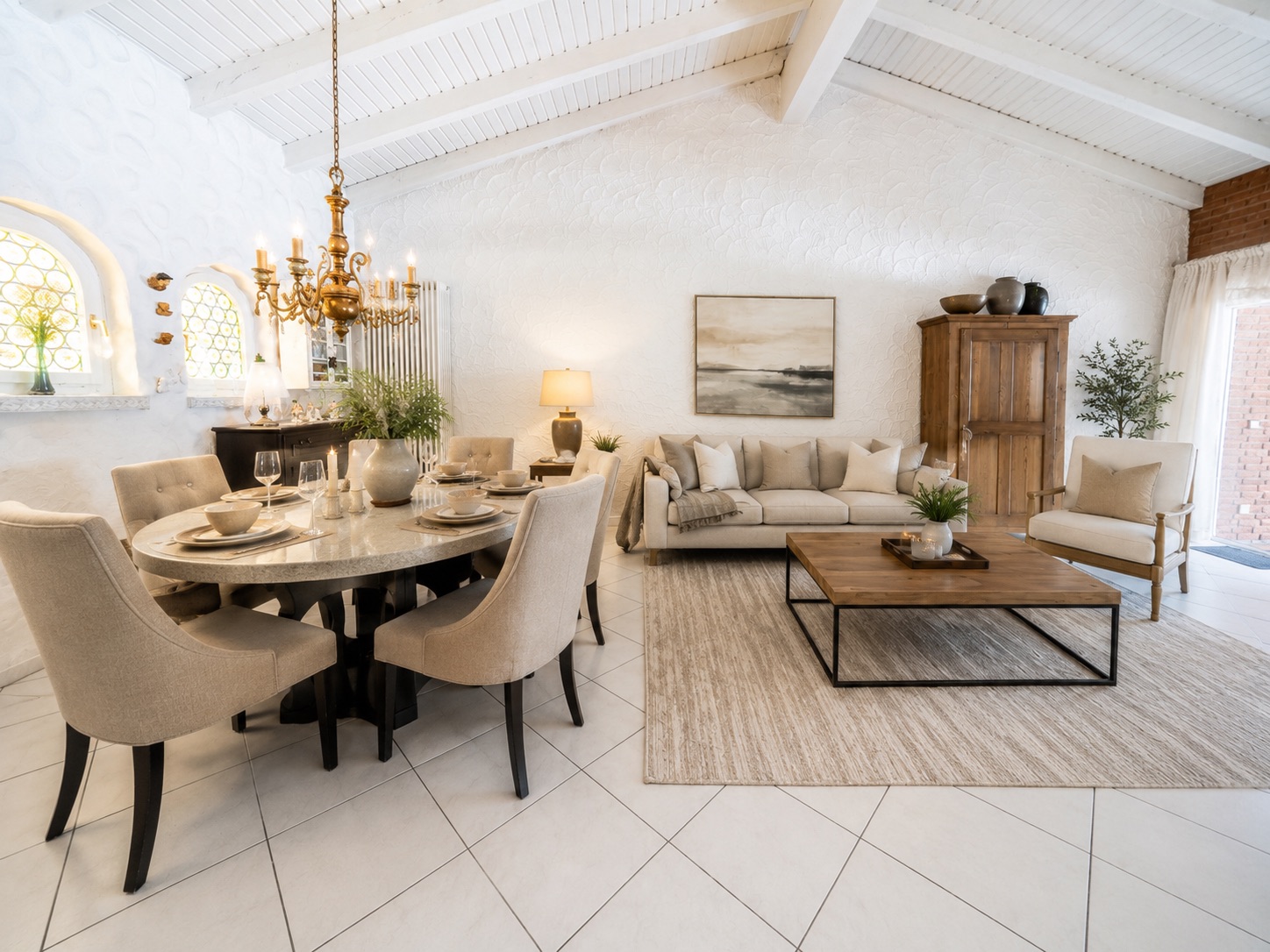 Helles Wohnzimmer mit Sofa, Esstisch und sechs Stühlen, Holztisch, Teppich und Kronleuchter.