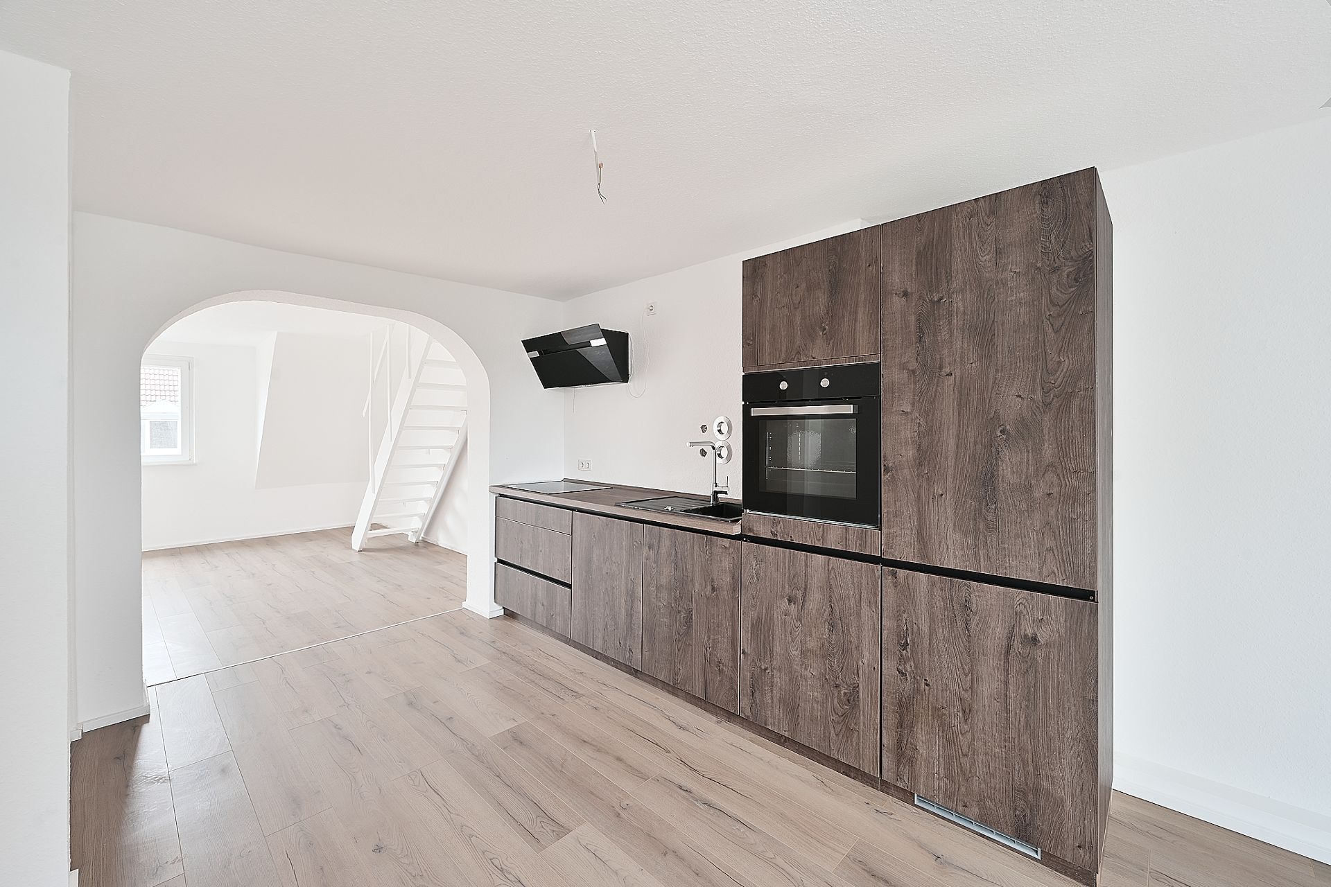 Moderne Einbauküche mit Holzfronten, offenem Durchgang und Treppe im hellen Raum.