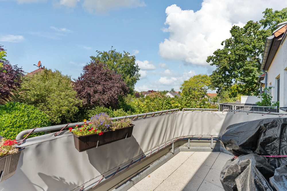 Balkon mit Blumenkästen am Geländer, Ausblick auf Bäume und Nachbarhäuser.