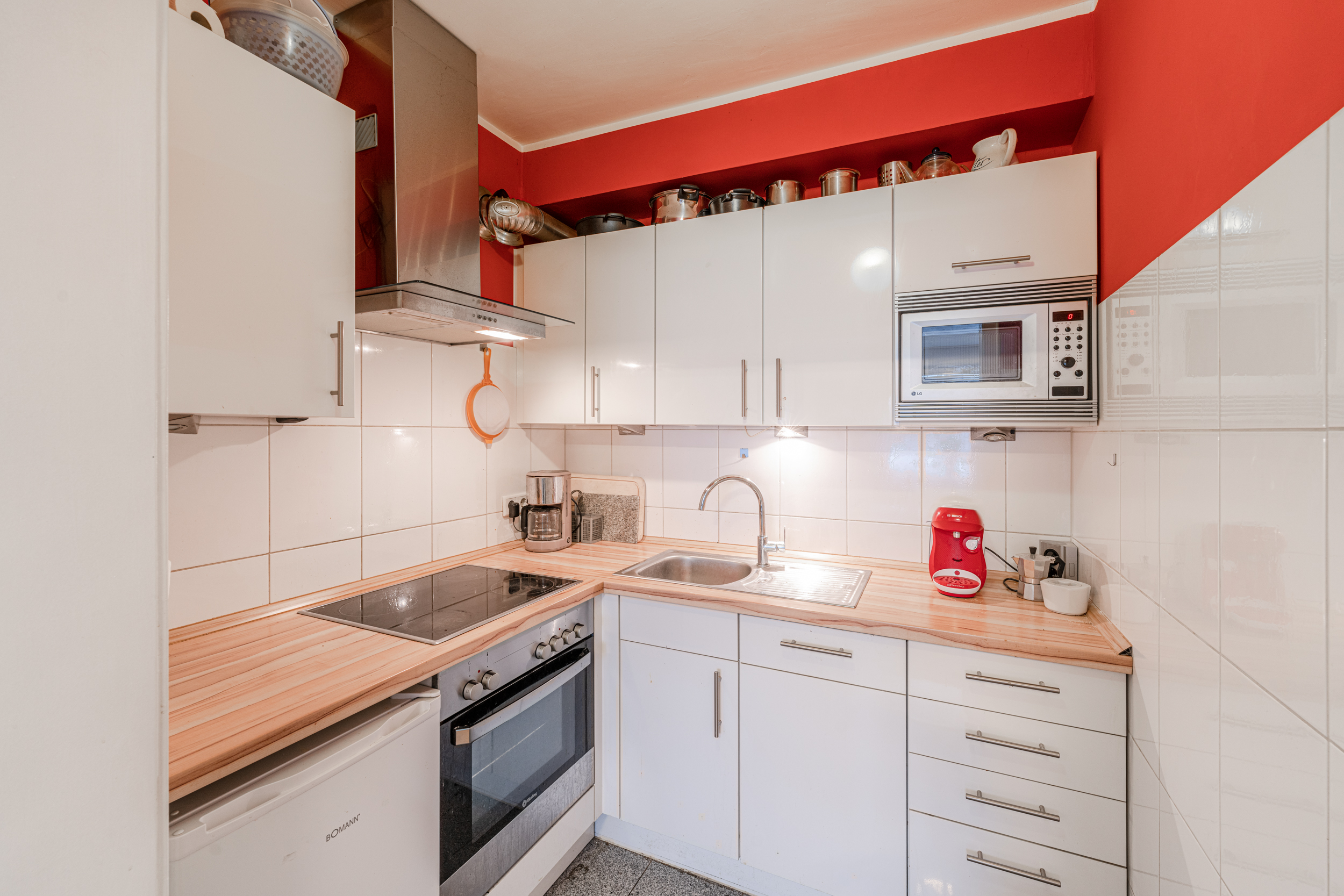 Moderne Küche mit weißen Schränken, Herd, Spüle, Kaffeemaschine und Mikrowelle.