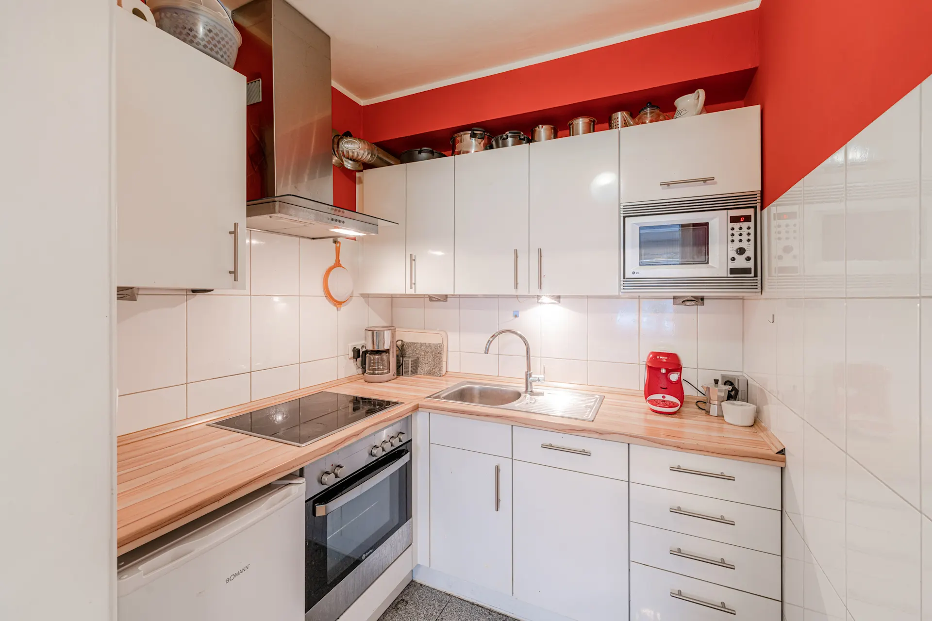 Moderne Küche mit weißen Schränken, Herd, Spüle, Kaffeemaschine und Mikrowelle.