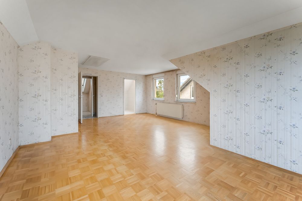 Leerer Raum mit Parkettboden, schräger Wand und zwei Fenstern, Tapeten mit Blumenmuster.