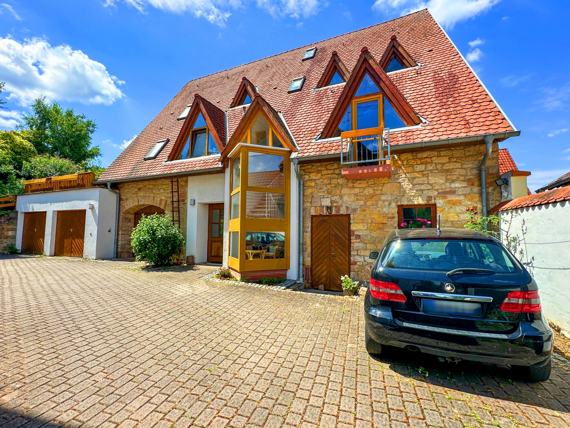 Wohnhaus mit rotem Dach, großen Fenstern und schwarzem Auto auf gepflastertem Hof.
