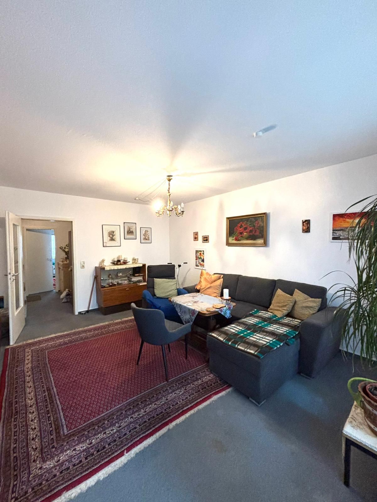 Wohnzimmer mit grauem Sofa, Teppich, Holztisch, Stuhl und Wandbildern.